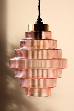 a pink glass light fixture hanging from a ceiling in front of a beige wall with shadows on it