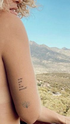 a woman with a small tattoo on her left arm and shoulder is looking out over the desert