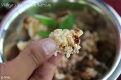 a hand holding food over a metal bowl