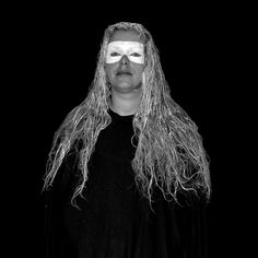 a man with long hair and white makeup wearing a black shirt is standing in front of a dark background