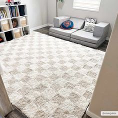 a living room with a gray couch and white rugs on the floor in front of a bookshelf