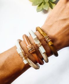 a woman's arm with four different bracelets on top of it and flowers in the background