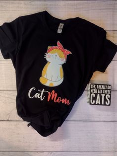 This crazy cool "Cat Mom" graphic is a full color DTF design, pressed onto a T Shirt.  The Gildan G500L Women's t-shirt is the perfect choice for a basic t-shirt designed for her. The 100% jersey knit cotton absorbs moisture, making this a great choice to wear as an undershirt or by itself on warm days. The long, loose length of the shirt provides you with carefree bending, flexing, and moving. *Care instructions:- Turn inside out and machine wash on cool or warm setting. It is preferable to hang dry for longest life, but can be machine dried on low setting. Do NOT iron the design. It will melt. Use a pressing cloth. **Please see the size chart** We do not accept returns or exchanges Cute Black T-shirt With Cat Design, Trendy Black T-shirt For Gift, Trendy Black T-shirt With Cat Print, Funny Black T-shirt With Cat Design, Novelty Black T-shirt As A Gift, Novelty Black T-shirt For Gift, Novelty Black T-shirt As Gift, Funny Black Top With Cat Design, Casual Cat Design T-shirt As Gift