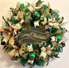 a christmas wreath with green and gold decorations on it that says merry christmas written across the front