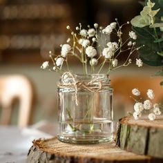 a glass jar filled with white flowers on top of a wooden table next to a tree stump