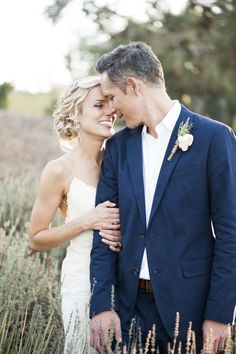 a bride and groom standing in the middle of tall grass with their arms around each other