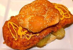 a fried chicken sandwich with pickles and cheese on a white plate, ready to be eaten