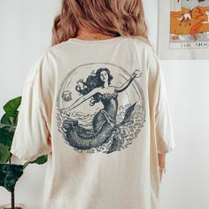 Get ready to show your style with our back designed Vintage Mermaid T-Shirt! Perfect for a beach party, concert or or just a casual day out, this graphic tee is a must-have.  Proudly Printed on Comfort Colors® tees, for that insanely soft, vintage look and feel.  Without doubt, this will be your favorite shirt. With its vintage-inspired design, this shirt is perfect for those who love a boho, western, or retro look. The oversized fit and soft, comfortable fabric make it the perfect choice for a Cotton Mermaid Top For Summer, Mermaid Shirts, Mermaid Tshirt, Mermaid Shirt, Vintage Mermaid, Comfort Colors Tee, Mermaid Birthday, Vintage Inspired Design, Feminine Look