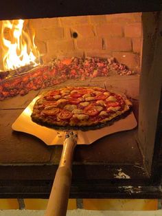 a pizza is being cooked in an outdoor oven with flames coming from the brick wall