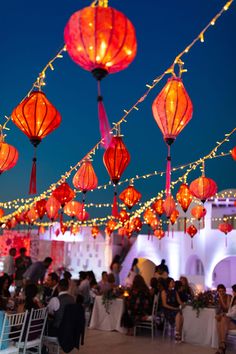 many red lanterns hanging from the ceiling and people sitting at tables in front of them