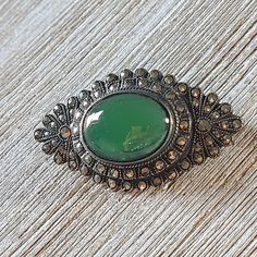 "Gorgeous Vintage Art Deco Brooch! Appears to be 1930's/1940's  It's definitely an older piece. The brooch features sparkly marcasite in sterling silver with a green glass stone. We aren't able to test the stone to be 100% sure of what it is. The brooch is marked sterling.  Measures 1-1/2\" length and 1\" width.  Great vintage condition. Does show signs of age and use. The clasp works perfectly but the pin is a bit bent. Clean and will need more cleaning/ polishing. See all photos. If you have a Art Deco Cabochon Brooches Collectible, Collectible Art Deco Cabochon Brooches, Vintage Oval Brooch With Cabochon, Vintage Oval Cabochon Brooch, Victorian Green Collectible Brooches, Handmade Art Deco Collectible Brooch, Handmade Art Deco Collectible Brooches, Vintage Green Brooch For Formal Occasion, Green Vintage Brooch For Formal Occasions