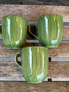 two green mugs sitting on top of a wooden bench