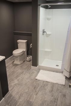 a white toilet sitting next to a shower in a bathroom on top of a hard wood floor