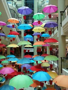 there are many colorful umbrellas hanging from the ceiling in this shopping mall, which is filled with people