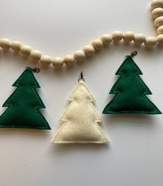 three felt christmas trees are hanging from a beaded necklace