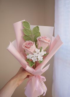 a person holding a bouquet of flowers with pink ribbon and green leaves on the stems