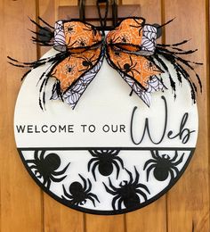 a welcome to our door sign with spider webs and orange bow hanging on the front door