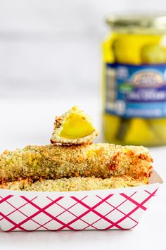 two pieces of food sitting in a paper container next to a jar of pickles