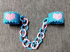 two pieces of beaded jewelry sitting on top of a gray cloth covered floor next to each other