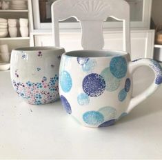 two cups sitting on top of a white table next to each other with blue and pink designs