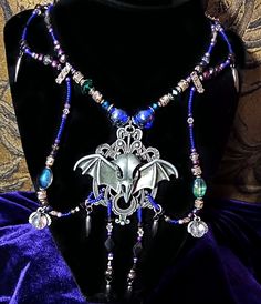 Unveil your gothic elegance with this stunning Steampunk Bat Pendant Necklace, a perfect blend of dark fantasy and intricate craftsmanship. This unique piece features a detailed bat pendant, capturing the essence of steampunk with its mechanical wings and ornate design. The necklace is adorned with a mix of vibrant blue and purple beads, complemented by antique silver-tone accents and emerald green details, adding a touch of mystical allure. The centerpiece bat pendant is crafted from high-quali Gothic Metal Jewelry For Fantasy Events, Steampunk Jewelry For Halloween Festival, Fantasy Necklaces For Halloween Festival, Gothic Choker Necklaces For Cosplay, Fantasy Halloween Choker Necklace, Gothic Metal Necklace, Gothic Metal Jewelry With Dragon Design, Steampunk Metal Necklaces For Festivals, Steampunk Metal Necklace For Festivals