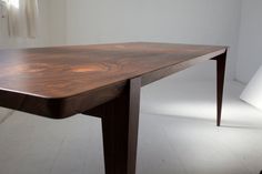 a wooden table sitting on top of a white floor next to a chair and wall