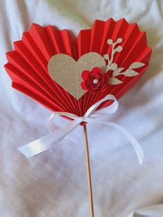 a red paper fan with a heart and flower on it sitting on a white sheet