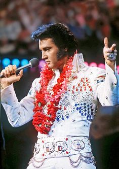 elvis presley performing on stage with microphone and leion garland around his neck, in front of an audience