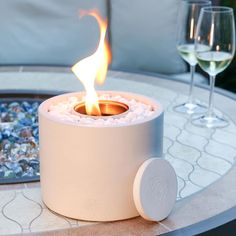 a fire pit sitting on top of a table next to two glasses of white wine