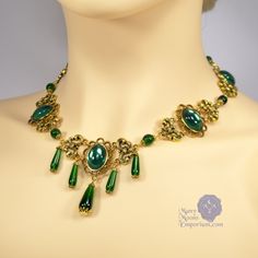 Marquise Xanthe Antique Gold and Emerald Green Edwardian Necklace Transform your cosplay and re-enactments from simple to exquisite with the Marquise Xanthe gold and green Edwardian necklace. It is as opulent as it is gorgeous. This stunning jeweled necklace features beautiful teardrops of emerald green glass capped with antique filigree as a focal. Equally entrancing, an oval emerald green gem framed in antique gold completes the focal with swirling gold scrolling which repeats around the lengt Edwardian Necklace, Medieval Belt, Your Cosplay, Antique Filigree, Acrylic Gems, Jewel Necklace, Gold And Green, Green Gems, Edwardian Fashion