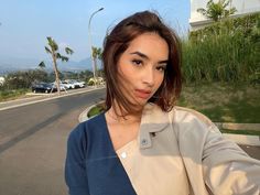 a woman taking a selfie in front of a street with cars and palm trees