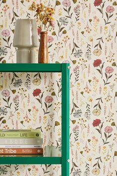 a green shelf with books on it next to a wallpapered wall and vase