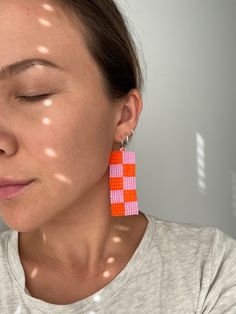 a woman with her eyes closed wearing orange and pink squares dangling from the back of her ear