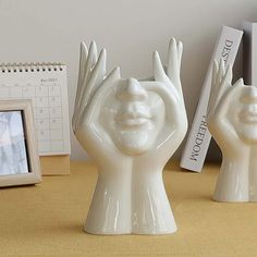 two white ceramic hands with faces on them are shown next to a calendar and an empty photo frame