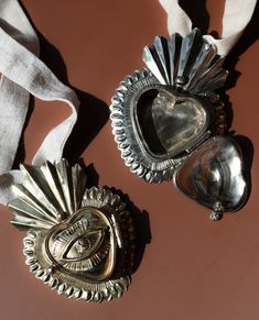 two silver heart shaped brooches sitting next to each other on top of a table