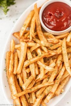 french fries on a plate with ketchup and parsley in the bowl next to it