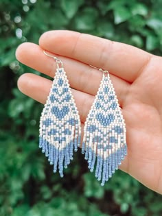 a hand holding a pair of blue and white beaded earrings