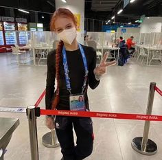 a woman wearing a face mask standing in front of a red barrier at an airport