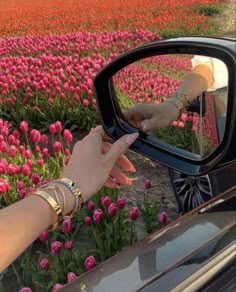 a woman's hand on the side mirror of a car in front of a field of tulips