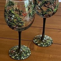 two wine glasses sitting on top of a wooden table covered in leaves and butterflies painted on them