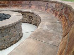 an outdoor fire pit surrounded by stone walls and paversed seating area with grass in the background