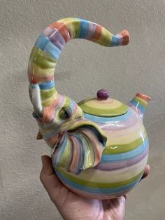 a hand holding a colorful striped tea pot