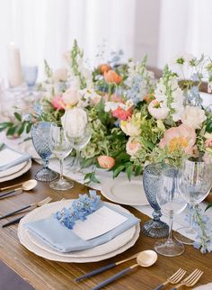 the table is set with blue and white place settings, silverware, and floral centerpieces