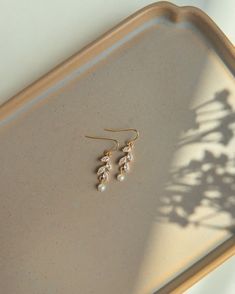 a pair of earrings sitting on top of a tray next to a shadow of a plant