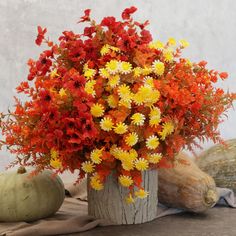 an arrangement of orange and yellow flowers in a wooden vase with pumpkins on the side