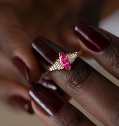 a close up of a person's hand wearing a ring with a pink stone