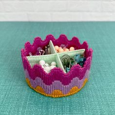 a pink, yellow and purple knitted container with lots of items in it on a blue surface