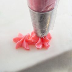 a close up of a pink substance in a cup on a white surface with red flowers