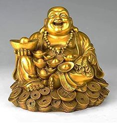 a golden buddha statue sitting on top of a pile of coins and holding a bowl