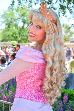 a woman with long blonde hair wearing a pink dress and tiara smiling at the camera